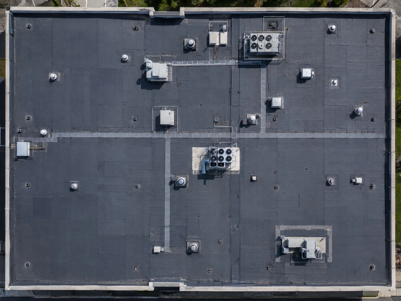 Top-down commercial rooftop showing mechanical units, drains, and seams.